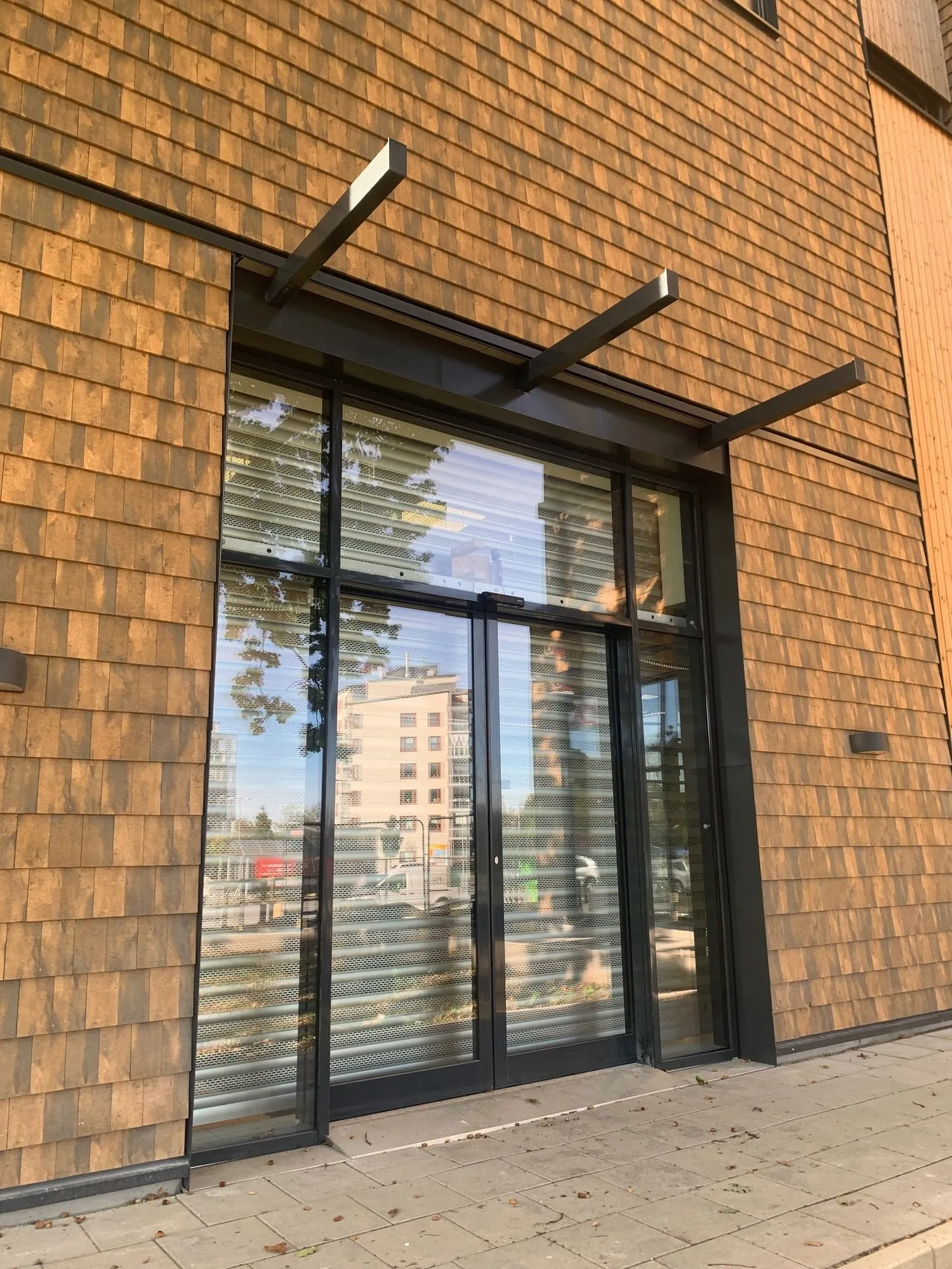 Entréparti med skjutdörr – Automatisk skjutdörr och sidopartier i mörk aluminium mot spånfasad. Injusterad och driftsatt med serviceavtal.