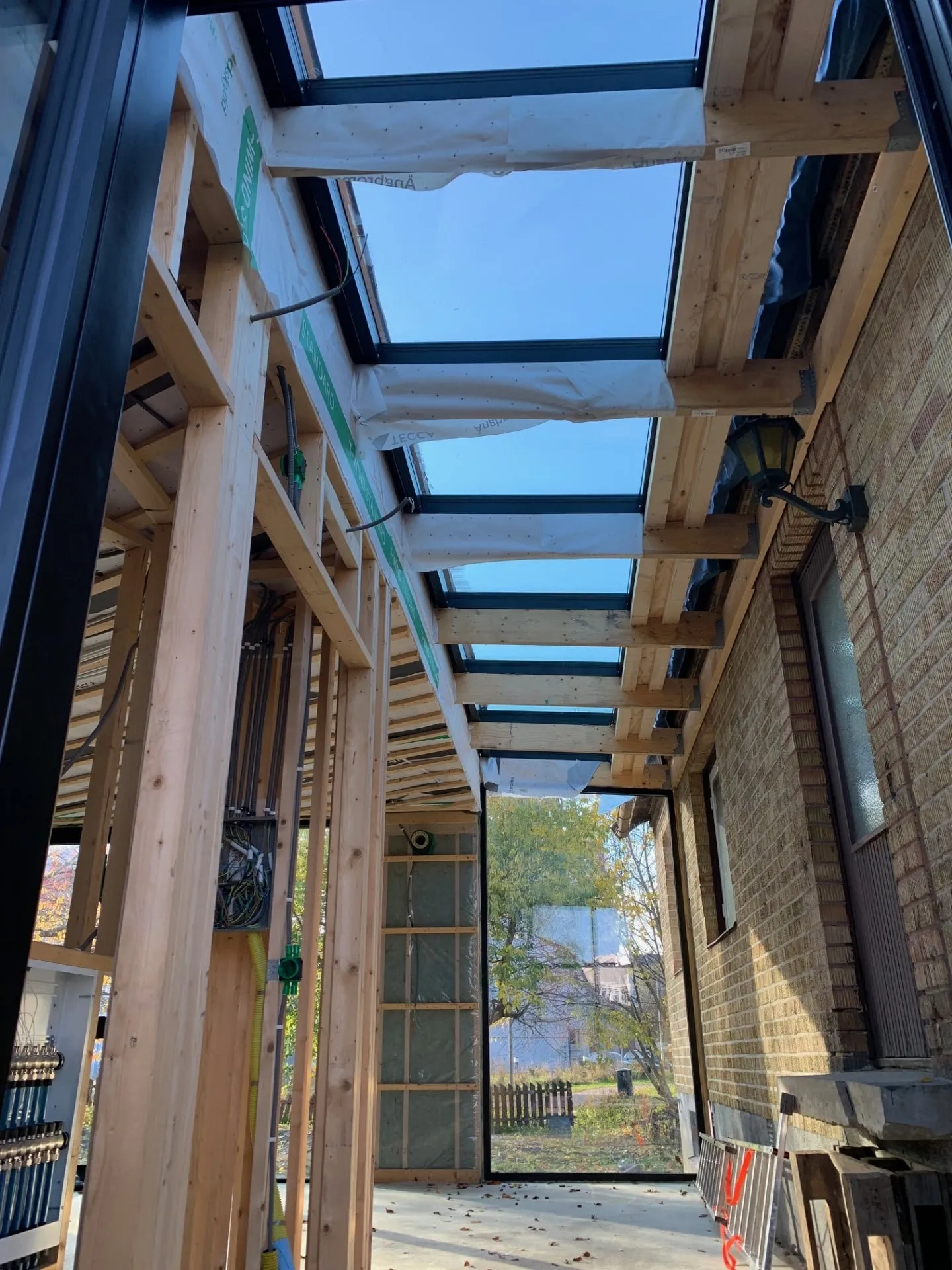 Glastak över entrégång – Glastak i limträstomme med laminerat säkerhetsglas, plus fasta glaspartier i gaveln. Vinklat för att leda av vatten och snö.