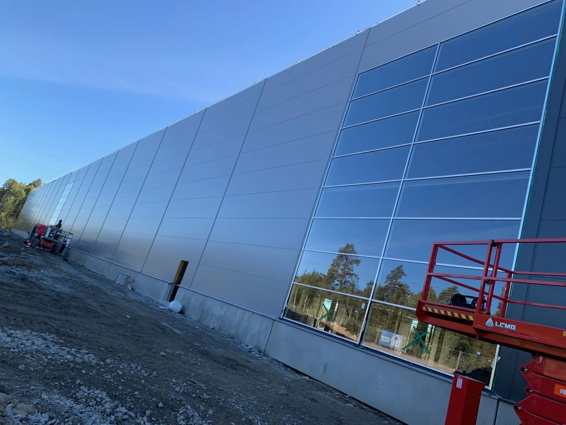 Fasadparti industribyggnad – Högt fasadparti i flera sektioner, monterat från saxlift mot plåtkassett. Härdat glas hela vägen upp till takfoten.